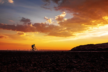 Fototapeta na wymiar Silhouette of cycling man on bike on beautiful sunset background
