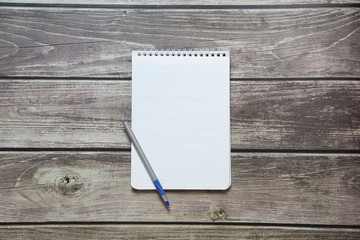 Notepad with a blank white sheet in a checker paper with ball pen lies on the background of wooden boards