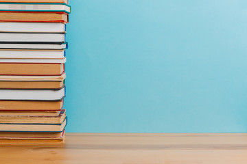 A simple composition of many hardback books, raw books on a wooden table and a bright blue background. Going back to school. Copy space. Education.