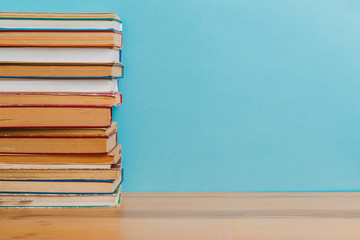 A simple composition of many hardback books, raw books on a wooden table and a bright blue background. Going back to school. Copy space. Education.