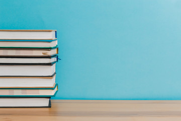 A simple composition of many hardback books, raw books on a wooden table and a bright blue background. Going back to school. Copy space. Education.