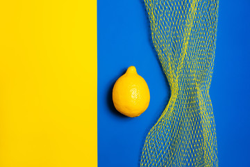 Whole lemon citrus fruit and yellow mesh packaging on bright color block background