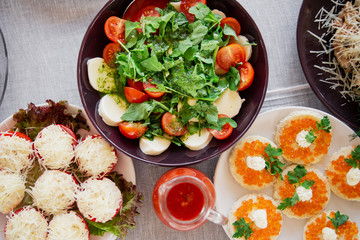 Stuffed tomatoes, sandwiches with caviar, fresh spring salad with cheese. Top view on the table