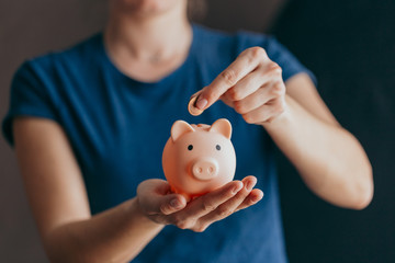 female hands hold a pink piggy bank and puts a coin there. The concept of saving money or savings,...