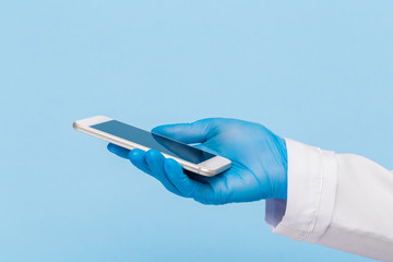 Female hand in a medical glove holds a blank modern mobile phone on a blue background. Mock up