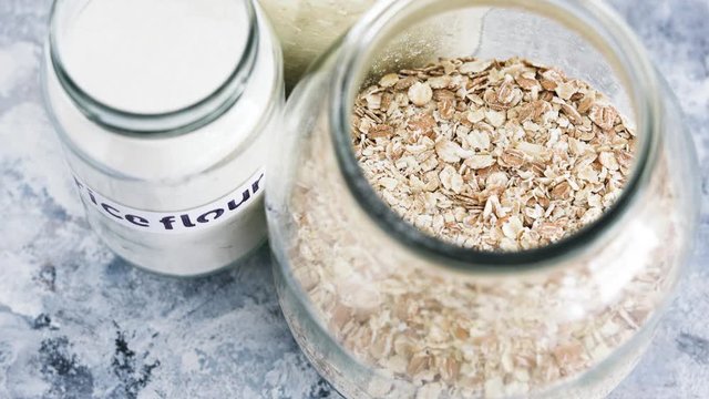 non-perishable food ingredients for vegan pantry, glass jars with oats flour and rice and camera panning vertically