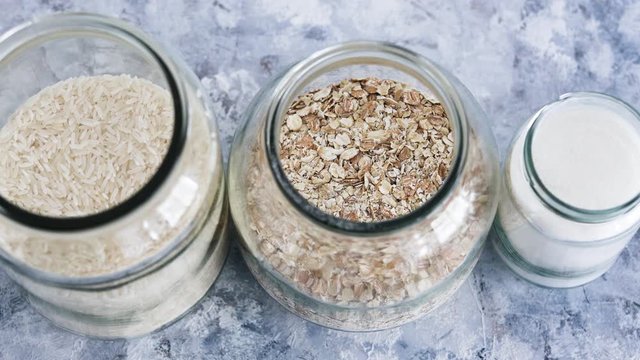 non-perishable food ingredients for vegan pantry, glass jars with oats flour and rice and camera defocusing
