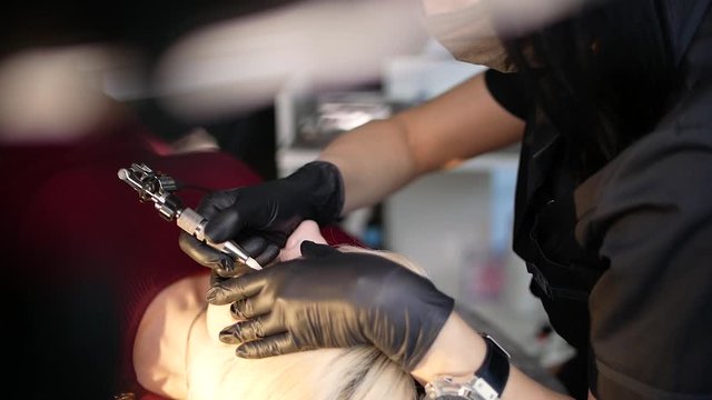 The cosmetologist begins the procedure correction of the shape of eyebrows in a beauty parlor. A method of permanent eyebrow tattoo correction. Microblading, eyebrow tatoo. Slow motion. Close up