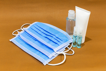 Bottle of antiseptic hand gel, alcohol and alcohol spray and Surgical ear-loop masks on brown background. Disease kill set for corona virus or covid-19 protection.