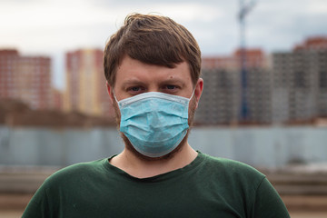 A young man in a medical mask on a stain background of houses under construction