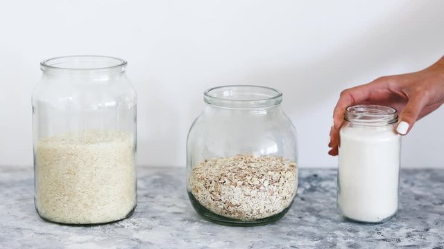 non-perishable pantry ingredients,glass jars with oats and rice andh hand placing flour next to them