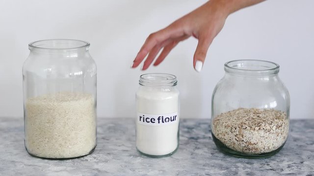 non-perishable pantry ingredients, glass jars with oats and rice andh hand placing rice flour among them