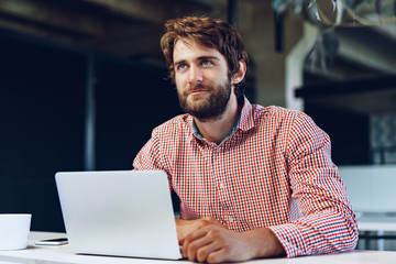 Portrait of young caucasian businessman using laptop computer at his workplace in modern office