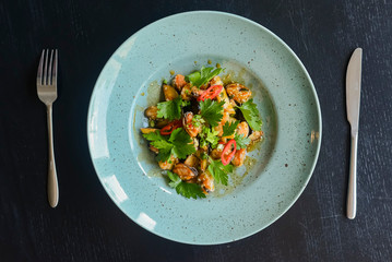 Salad with fresh grilled vegetables on a blue plate on black rustic wooden background.