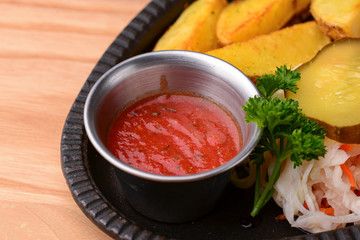 Grilled steak with vegetables and tomato sauce served on a black plate over light rustic background.