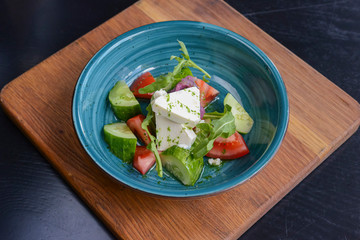 One plate of vegetable salad with feta cheese, cucumbers, tomatoes, and broccoli served in bowl on rustic wooden board.