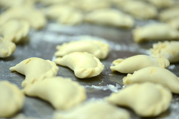 Fototapeta na wymiar Uncooked russian vareniki on metal tray with flour. Process of making vareniki.