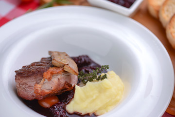 Mashed potato with meat and gravy served in a white plate over red plaid tablecloth.