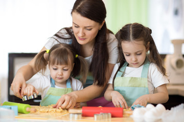 Mom with her 2 and 5 years old daughters are cooking in domestic kitchen to Mothers day