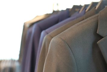 Closeup of gray man's suit with others  hanging on hangers in tailor shop. 