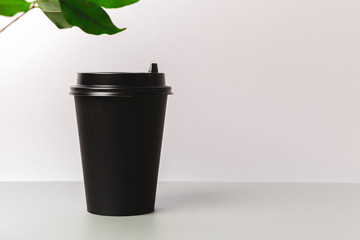 Disposable paper coffee cup and green leaf. Ecology concept