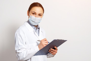 portrait of a female doctor in a protective mask with a clipboard and a pen in her hands, making a record.