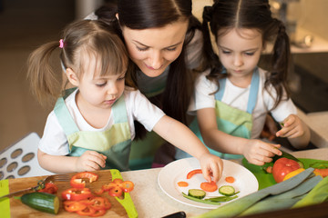 Happy family in the kitchen. Mom and kids daughters playing and having fun in the kitchen preparing.