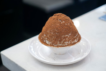 Chocolate Bingsu, Korean sweet dessert, milk shaved ice topped with cocoa powder on white plate.
