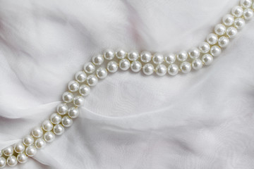 A necklace of pearls lies on a white cloth