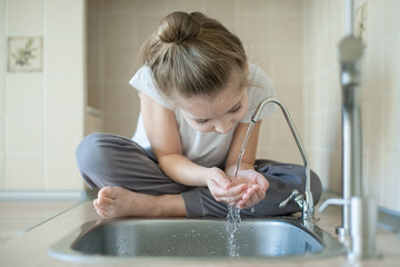 Caucasian little girl drinking from water tap or faucet in kitchen. Hands open for drinking tap...