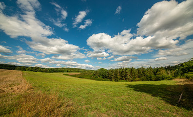 land view in small valley with field, meadow, forest and blue cloudy sky