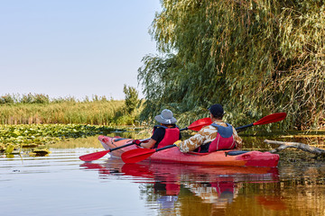 Couple man and a woman paddle in red kayak on a river. Back view on couple kayaking on a river at summer
