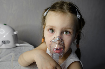 A child sits with an inhaler at home. Coronovirus treatment concept Covid19. Girl making inhalation...