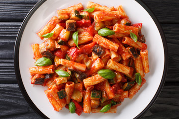 talian Pasta Tortiglioni with eggplant, zucchini, pepper and basil in tomato sauce close-up in a plate. Horizontal top view