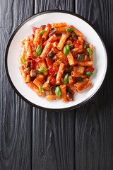 Tortiglioni pasta with eggplant, zucchini, pepper and basil in tomato sauce close-up in a plate. Vertical top view