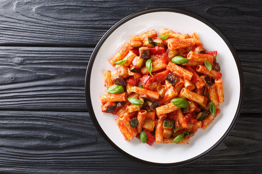 Tortiglioni pasta diet recipe with summer vegetables and basil in tomato sauce close-up in a plate. Horizontal top view