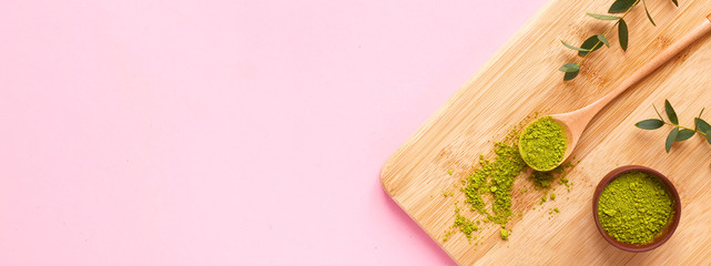 matcha tea on wooden cutting board with spoon and leaf on pink background. Banner. Concept healthy drink, detox, copyspace, flat lay.