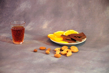 Crystal glass of cognac, next to a plate with lemon slices and chocolate on a gray background, a...