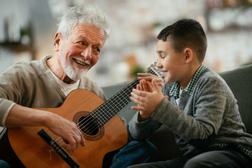 Grandpa and grandson playing guitar. Grandfather and grandson enjoying at home.