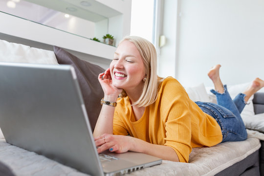 Young albino woman doing research work for her business. Smiling woman sitting on sofa while browsing online shopping website. Happy girl browsing through the internet during free time at home.