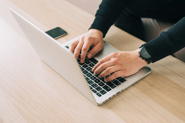 Man's hands using laptop with blank screen on desk in home interior. Mockup image white screen.