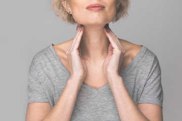 Female checking thyroid gland by herself. Close up of woman in white t- shirt touching neck with red spot. Thyroid disorder includes goiter, hyperthyroid, hypothyroid, tumor or cancer Health care. - obrazy, fototapety, plakaty