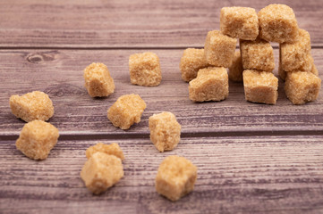 Pieces of brown cane sugar scattered on a wooden background. Close up.