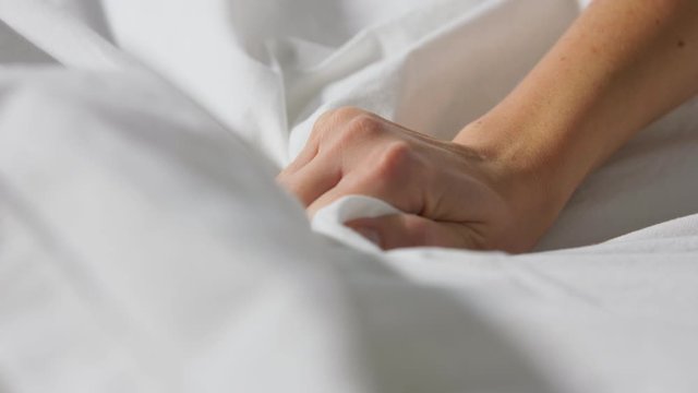 people and bedtime concept - hand of woman squeezing white bed linen or blanket