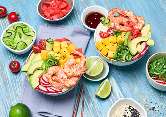 Hawaii shrimp poke, avocado, mango, rice, seaweed, cucumber, radish in bowl. Home made vegetarian prawn poke. Seafood concept. Asian shrimp poke salad on blue wood background.