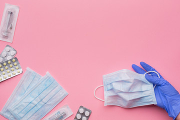 Medical protective masks, disposable syringes, pills and hand in latex glove on a pink background. The concept of protecting health from the virus. Copy space.