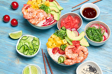 Fototapeta na wymiar Shrimp poke, avocado, mango, rice, seaweed, cucumber, radish in bowl. Home made vegetarian prawn poke. Seafood concept. Asian shrimp poke salad on blue wood background.