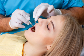 Beautiful woman with healthy straight white teeth sitting at dental chair with open mouth during oral checkup while doctor working at teeth