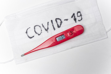 Thermometer on the surgical mask. High temperature as a main symptom of virus infection. Covid-19.