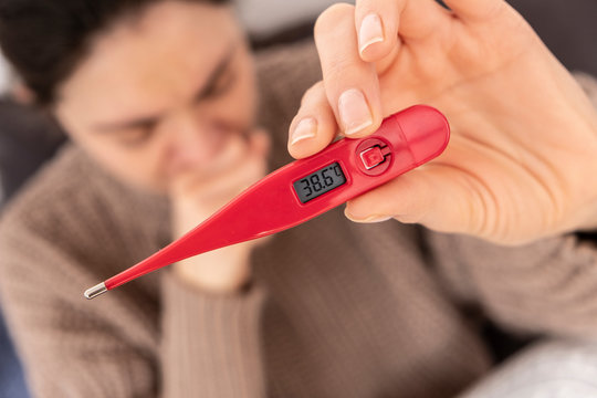 Young woman has a fever. She is holding a thermometer and caughing on the fist, to don't transmite a virus.